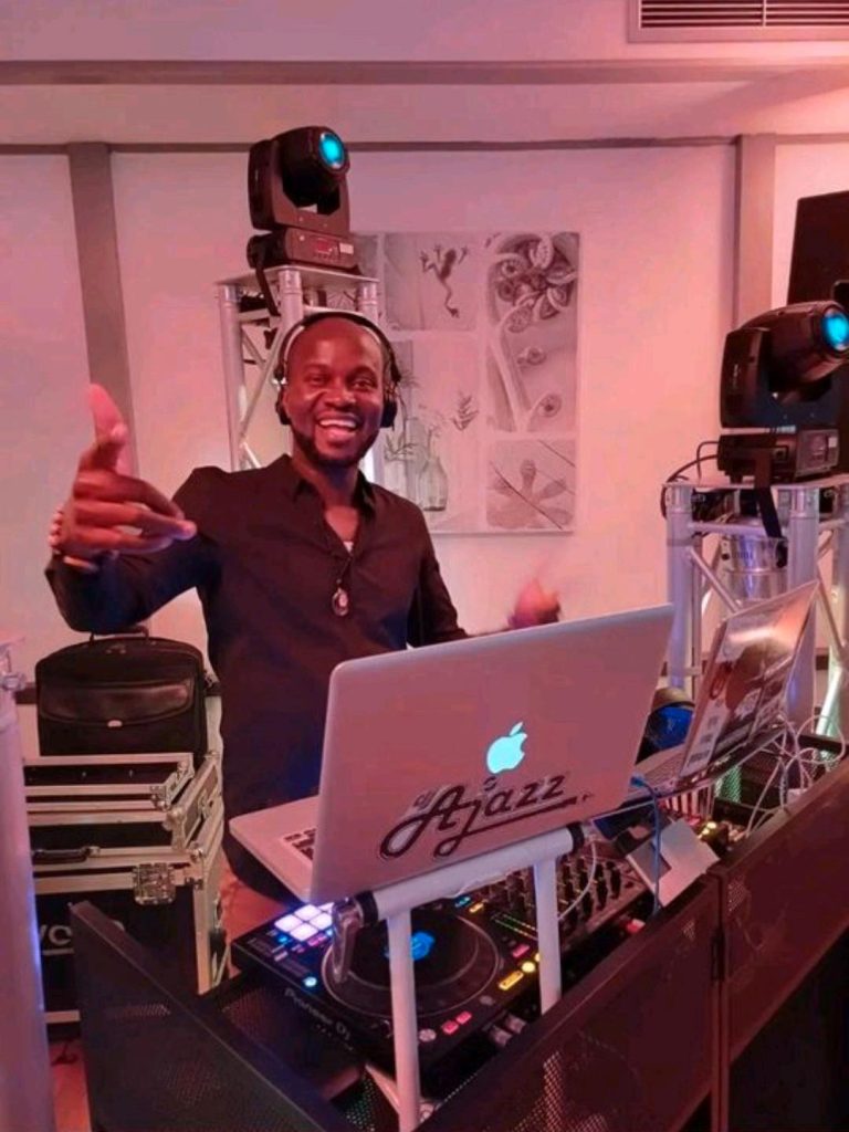 DJ Ajazz lächelt mit Kopfhörern und Beleuchtung im Hintergrund.