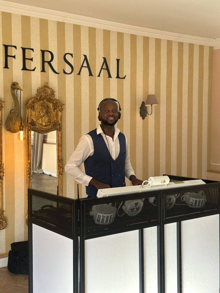 DJ Ajazz im Hemd mit afrikanischem Muster hinter seinem Setup.