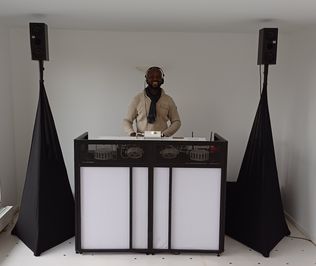 DJ Ajazz im Hemd mit afrikanischem Muster hinter seinem Setup.